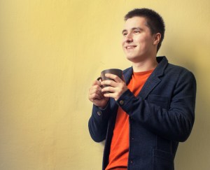Happy young business man drinking coffee near the wall